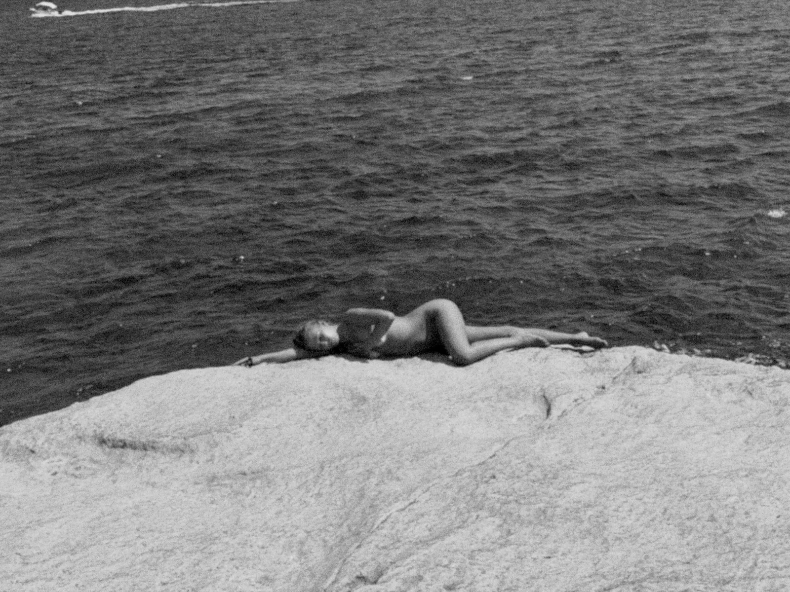 sofia lying on a flat rock at the edge of the sea, black and white