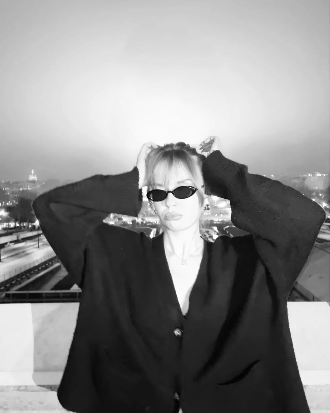 sofia with her hands in her hair, the city lights behind her, black and white