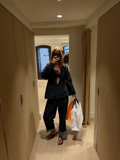 Mirror selfie in a hotel corridor, all in black, two shopping bags